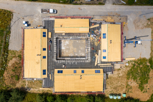 Igensdorf Germany 11 May 2024 Aerial view of a modern residential construction site with wooden roof structures arranged around a central courtyard under bright sunlight. Igensdorf Germany 11 May 2024 Aerial view of a modern residential construction site with wooden roof structures arranged around a central courtyard under bright sunlight.