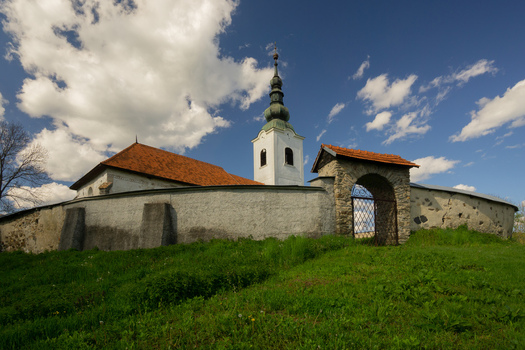 View of the historic Evangelical Church with its white bell tower and stone defensive wall under a cloudy blue sky in Rimavska Bana Banska Bystrica Region Slovakia. View of the historic Evangelical Church with its white bell tower and stone defensive wall under a cloudy blue sky in Rimavska Bana Banska Bystrica Region Slovakia.