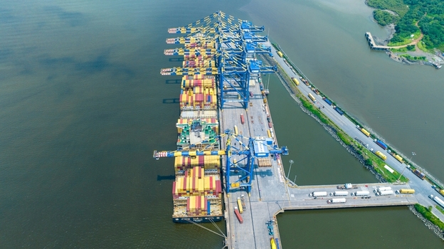 Aerial view of Jawaharlal Nehru Port Authority with a container ship docked at the pier featuring shipping containers industrial cranes and trucks in Juna Sheva Maharashtra India. Aerial view of Jawaharlal Nehru Port Authority with a container ship docked at the pier featuring shipping containers industrial cranes and trucks in Juna Sheva Maharashtra India.