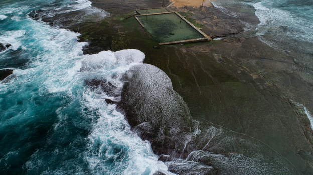 Aerial view of Newport Rock Pool with turquoise waves crashing against the rocky shore and white foam Sydney New South Wales Australia.