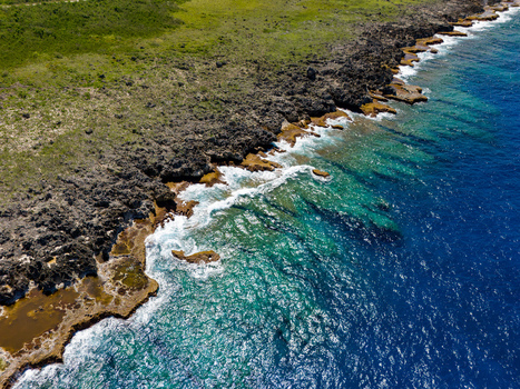 Aerial view of Chigit Beach with rugged volcanic rock formations turquoise coastal waters and lush green vegetation in Northern Tinian Tinian Northern Mariana Islands. Aerial view of Chigit Beach with rugged volcanic rock formations turquoise coastal waters and lush green vegetation in Northern Tinian Tinian Northern Mariana Islands.