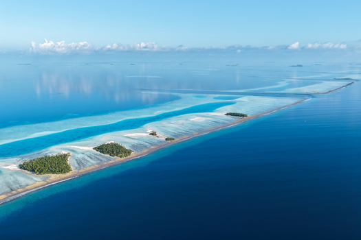 Aerial view of lush tropical islands with green palm trees and turquoise coral reefs surrounded by the deep blue ocean under a clear sky near Vaanee Dhaalu Atoll Maldives. Aerial view of lush tropical islands with green palm trees and turquoise coral reefs surrounded by the deep blue ocean under a clear sky near Vaanee Dhaalu Atoll Maldives.