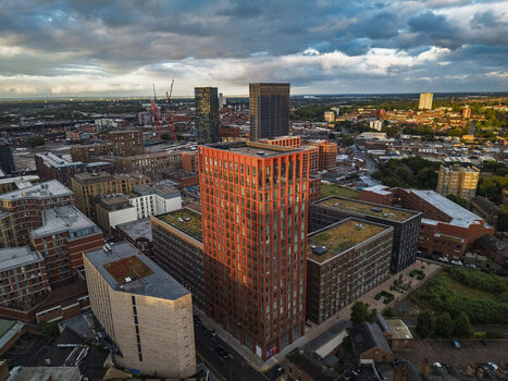 Aerial view of a modern red brick high rise building surrounded by urban architecture rooftops and green roofs in the city center of Birmingham England United Kingdom.
