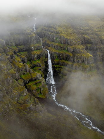Aerial view of a waterfall cascading down mossy basalt cliffs in the Eastern Region of Iceland. Aerial view of a waterfall cascading down mossy basalt cliffs in the Eastern Region of Iceland.