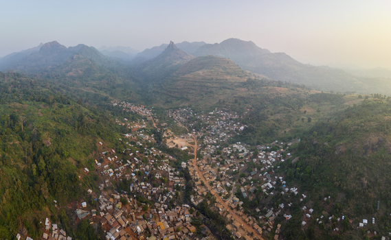 Aerial view of a town nestled in a lush valley surrounded by misty mountains and dense green forests under a hazy sky Man Montagnes District Cote d Ivoire.