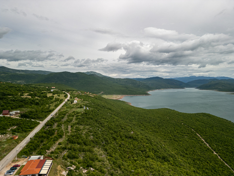 Aerial view of Bileca Lake surrounded by lush green hills a winding road and scattered houses under a cloudy sky in Bileca Republika Srpska Bosnia and Herzegovina. Aerial view of Bileca Lake surrounded by lush green hills a winding road and scattered houses under a cloudy sky in Bileca Republika Srpska Bosnia and Herzegovina.