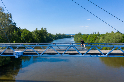 Aerial view of Sportinsel Forchheim featuring a blue bridge over the river with a person sitting on the railing and lush green trees Forchheim Bayern Germany.