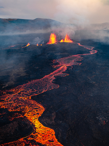Aerial view of a volcanic eruption with glowing lava flowing through a dark landscape in Iceland. Aerial view of a volcanic eruption with glowing lava flowing through a dark landscape in Iceland.