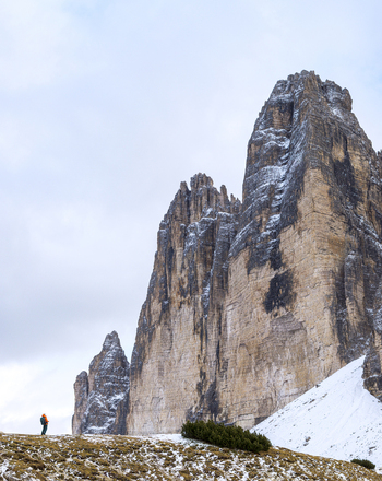 Aerial view of Tre Cime di Lavaredo their snow dusted faces contrasting with the golden grass below a lone figure adding scale to the imposing landscape Dolomites Italy.