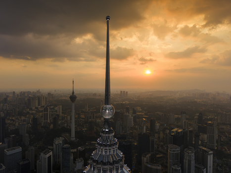 Kuala Lumpur Malaysia 11 March 2026 Aerial view of the spire of the Petronas Twin Towers and the KL Tower against a dramatic sunset sky with orange clouds over the city skyline.
