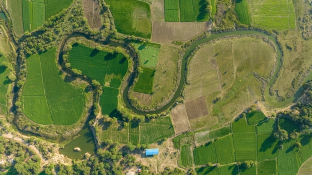 Aerial view of a winding river flowing through lush green agricultural fields and small plots of land with a small blue roofed building in Nagda Madhya Pradesh India. Aerial view of a winding river flowing through lush green agricultural fields and small plots of land with a small blue roofed building in Nagda Madhya Pradesh India.