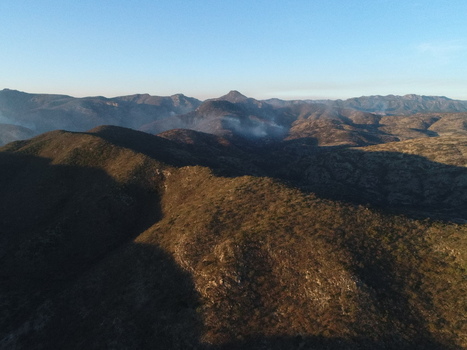 Aerial view of the Sierra de San Miguelito mountain range with smoke from a wildfire rising above the dry rugged terrain under a clear sky in San Luis Potosi San Luis Potosi Mexico.