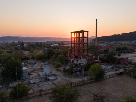 Aerial view of an abandoned industrial factory with a skeletal structure and tall chimney at sunset surrounded by trees and dry fields in Velingrad Pazardzhik Bulgaria. Aerial view of an abandoned industrial factory with a skeletal structure and tall chimney at sunset surrounded by trees and dry fields in Velingrad Pazardzhik Bulgaria.