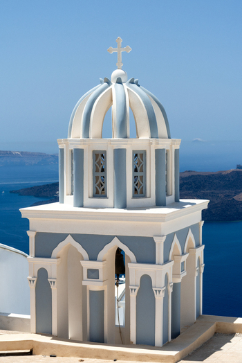 View of the iconic blue domed church bell tower with intricate white arches and a cross set against the deep blue Aegean Sea in Fira Greece. View of the iconic blue domed church bell tower with intricate white arches and a cross set against the deep blue Aegean Sea in Fira Greece.
