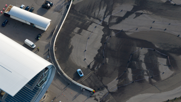 Aerial view of a light blue car driving on a track marked by tires at the Hockenheimring circuit with a modern grandstand and parked vehicles in Hockenheim Baden Wurttemberg Germany. Aerial view of a light blue car driving on a track marked by tires at the Hockenheimring circuit with a modern grandstand and parked vehicles in Hockenheim Baden Wurttemberg Germany.