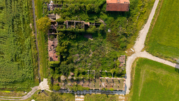 Aerial view of an abandoned farm with overgrown vegetation crumbling brick structures and surrounding green fields in Milan Lombardy Italy.