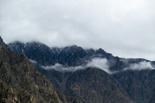 View of rugged mountain peaks partially covered in snow and shrouded in thick white clouds under an overcast sky Chilas Gilgit Pakistan. View of rugged mountain peaks partially covered in snow and shrouded in thick white clouds under an overcast sky Chilas Gilgit Pakistan.