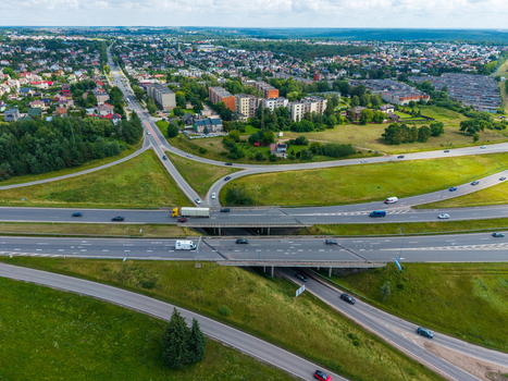 Aerial view of a highway interchange with vehicles driving on roads surrounded by green fields and residential buildings in Kaunas Kaunas County Lithuania.