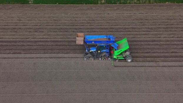 Aerial view of a blue tractor planting potatoes in a brown field Netherlands.