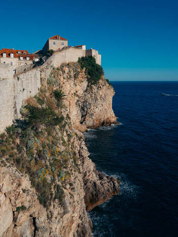 View of the historic stone walls of Dubrovnik Old Town perched on a rugged cliff above the deep blue Adriatic Sea Dubrovnik Dubrovnik Neretva County Croatia. View of the historic stone walls of Dubrovnik Old Town perched on a rugged cliff above the deep blue Adriatic Sea Dubrovnik Dubrovnik Neretva County Croatia.