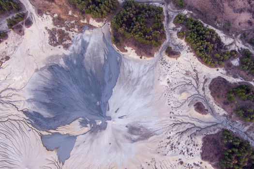 Aerial view of the Mud Volcanoes of Paclele Mari featuring unique grey mud flows and intricate drainage patterns surrounded by pine forests in Paclele Buzau County Romania.