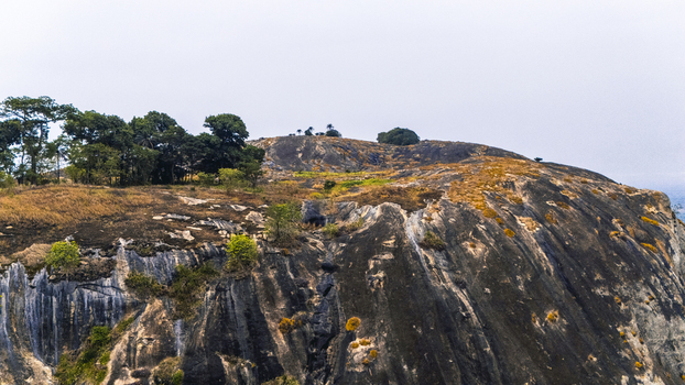 Aerial view of a dramatic rocky outcrop crowned with sparse trees and dry grass under a muted sky at Iyake Lake Oyo Nigeria. Aerial view of a dramatic rocky outcrop crowned with sparse trees and dry grass under a muted sky at Iyake Lake Oyo Nigeria.