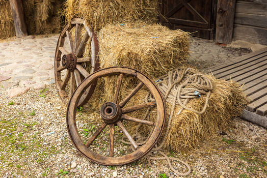 View of two vintage wooden cart wheels leaning against stacked hay bales and a thick rope on a stone path in Taujenai Vilnius County Lithuania.