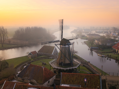 Aerial view of the historic De Kaai windmill standing on a grassy bastion by a canal during a misty sunrise in Sloten Friesland Netherlands. Aerial view of the historic De Kaai windmill standing on a grassy bastion by a canal during a misty sunrise in Sloten Friesland Netherlands.
