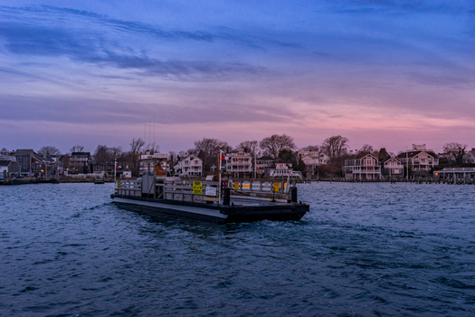 View of the Chappaquiddick ferry crossing the harbor with coastal houses and a twilight sky in Edgartown Massachusetts United States.