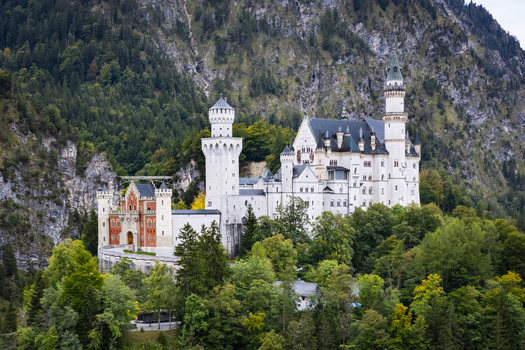 Aerial view of Neuschwanstein Castle a majestic fortress with ornate towers and warm colored walls perched atop a verdant forested hill Neuschwanstein Castle Bayern Germany. Aerial view of Neuschwanstein Castle a majestic fortress with ornate towers and warm colored walls perched atop a verdant forested hill Neuschwanstein Castle Bayern Germany.