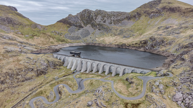 Aerial view of a dramatic dam holding back the still dark waters contrasting with the rugged mountainous terrain under a cloudy sky Blaenau Ffestiniog Wales United Kingdom. Aerial view of a dramatic dam holding back the still dark waters contrasting with the rugged mountainous terrain under a cloudy sky Blaenau Ffestiniog Wales United Kingdom.