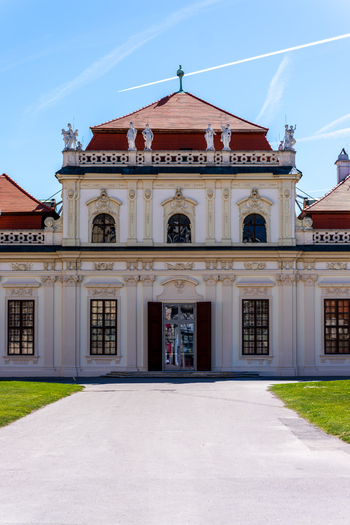 View of the baroque facade of Belvedere Palace with ornate statues on the roof and a gravel path under a clear blue sky in Vienna Austria. View of the baroque facade of Belvedere Palace with ornate statues on the roof and a gravel path under a clear blue sky in Vienna Austria.