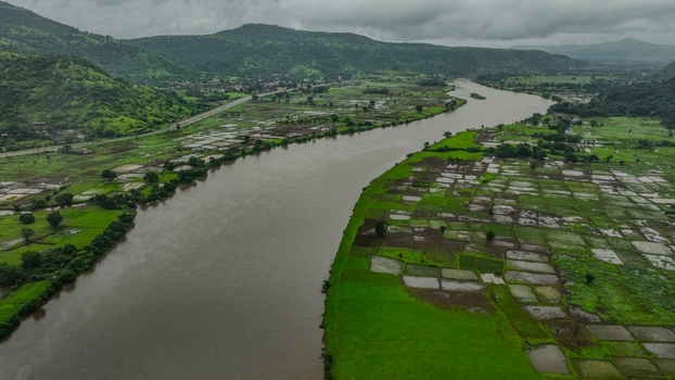 Aerial view of the Savitri River flowing through lush green rice paddies and agricultural fields near the Mumbai Goa Highway in Mahad Maharashtra India.