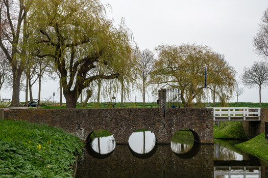 View of the historic stone bridge at Radboud Castle with circular arches reflecting in the moat water and weeping willow trees in Medemblik Noord Holland Netherlands. View of the historic stone bridge at Radboud Castle with circular arches reflecting in the moat water and weeping willow trees in Medemblik Noord Holland Netherlands.