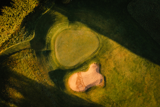 Aerial view of a golf course green and sand bunker illuminated by golden hour light with long shadows in Valmiera Valmiera Latvija.