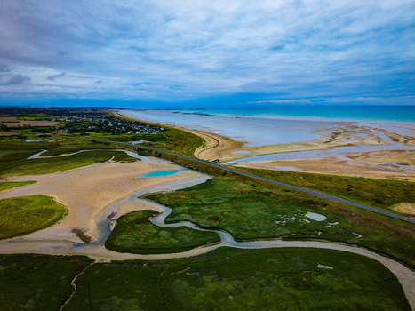 Aerial view of the Havre de Geffosses featuring winding tidal channels lush green salt marshes and a sandy coastline under a cloudy sky in Geffosses Normandy France.
