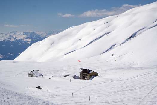 Aerial view of Colle del Piccolo San Bernardo with snow covered mountain huts and paragliders under a clear blue sky in La Thuile Valle d Aosta Italy. Aerial view of Colle del Piccolo San Bernardo with snow covered mountain huts and paragliders under a clear blue sky in La Thuile Valle d Aosta Italy.