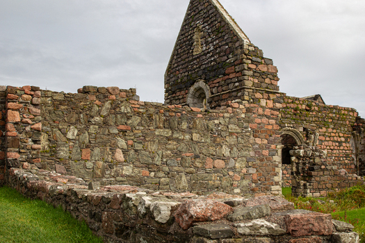 View of the ancient stone ruins of Iona Nunnery with weathered masonry walls and arched windows under a cloudy sky in Baile Mor Scotland United Kingdom. View of the ancient stone ruins of Iona Nunnery with weathered masonry walls and arched windows under a cloudy sky in Baile Mor Scotland United Kingdom.