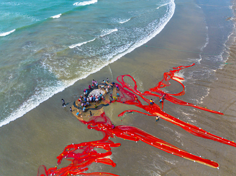 Cox s Bazar Bangladesh 10 March 2026 Aerial view of a vibrant red fishing net sprawled across the sandy beach contrasting with the turquoise waves and the bustling activity of local fishermen.