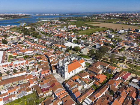 Aerial view of the striking white church contrasting against the red tiled roofs of the buildings framed by the blue river and distant horizon Vila Franca de Xira Portugal. Aerial view of the striking white church contrasting against the red tiled roofs of the buildings framed by the blue river and distant horizon Vila Franca de Xira Portugal.