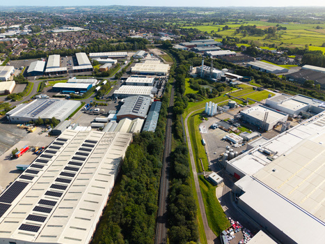 Aerial view of industrial warehouses and factory buildings with solar panels on rooftops separated by a railway line and green fields in Lisburn Northern Ireland United Kingdom. Aerial view of industrial warehouses and factory buildings with solar panels on rooftops separated by a railway line and green fields in Lisburn Northern Ireland United Kingdom.