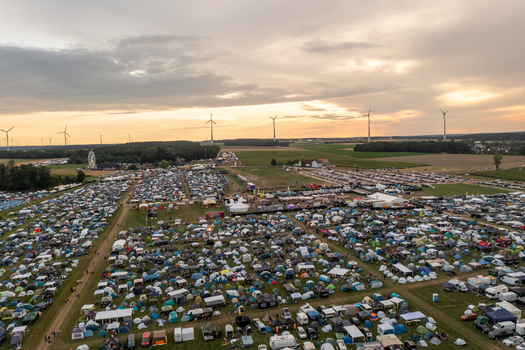 Aerial view of the Open Beatz Festival campsite with thousands of tents a Ferris wheel and wind turbines under a sunset sky Herzogenaurach Bayern Germany. Aerial view of the Open Beatz Festival campsite with thousands of tents a Ferris wheel and wind turbines under a sunset sky Herzogenaurach Bayern Germany.
