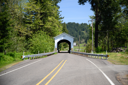View of a white covered bridge on a rural road surrounded by lush green trees and forest in Washington USA. View of a white covered bridge on a rural road surrounded by lush green trees and forest in Washington USA.