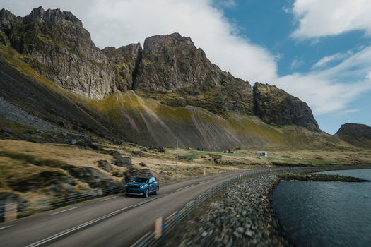 Aerial view of a blue car driving along the coastal road near the dramatic Stokksnes mountains in Iceland.