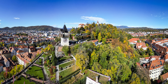 Aerial view of the Grazer Uhrturm clock tower on Schlossberg hill amidst a tapestry of autumnal colors under a clear sky Graz Styria Austria.