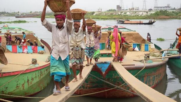 View of workers carrying sand baskets from boats in Dhaka Bangladesh.
