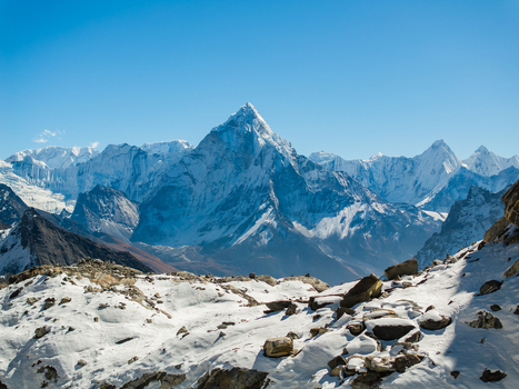 Aerial view of the snow capped Ama Dablam mountain peak rising above the rugged Himalayan landscape under a clear blue sky in Nepal.