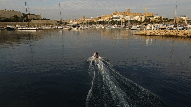Aerial view of a small motorboat leaving a harbor filled with yachts with historic stone buildings and fortifications in the background Malta. Aerial view of a small motorboat leaving a harbor filled with yachts with historic stone buildings and fortifications in the background Malta.