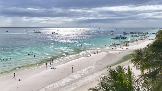 Malay Philippines 02 May 2026 Aerial view of Boracay Island with turquoise waters numerous boats anchored offshore and people enjoying the white sand beach under a cloudy sky.