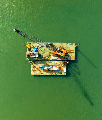 Aerial view of a construction crane mounted on a floating barge with a small support boat in the calm green waters of Williamstown Victoria Australia. Aerial view of a construction crane mounted on a floating barge with a small support boat in the calm green waters of Williamstown Victoria Australia.